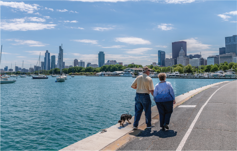 mature adult couple walking along lakefront trail with small dog on leash